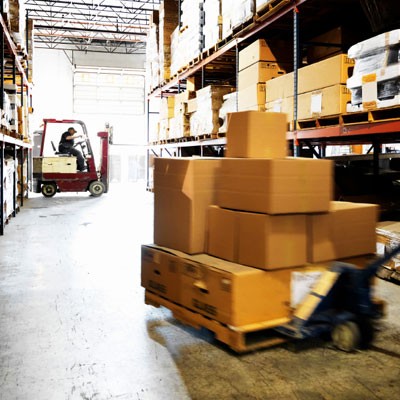 A photo of a warehouse with boxes on a rolling jack and a forklift in the background.